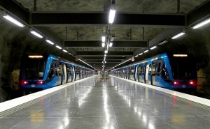 Two blue local trains leave an empty platform in an underground looking interieur. Photo.