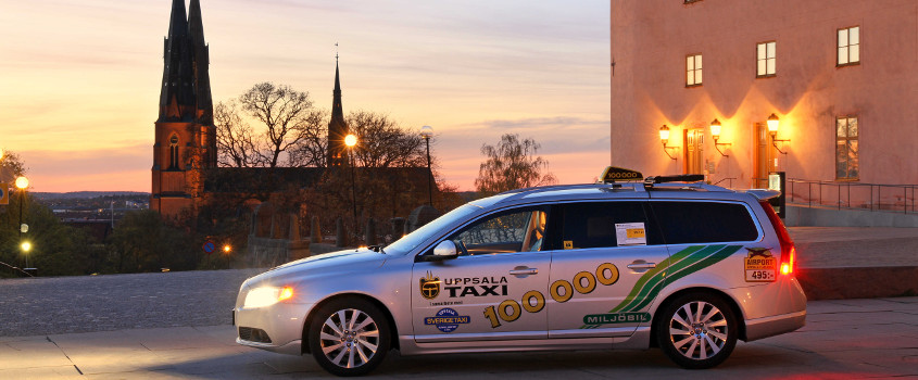 A car marked Uppsala Taxi parked in front of the silhouette of Uppsala Cathedral. Photo.